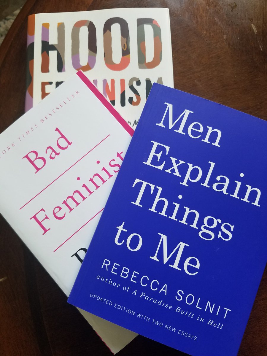 Three books sitting on a mahogany wood coffee table. The books are "Hood Feminism," "Bad Feminist," and "Men Explain Things To Me." The first is a hardcover and the other two are paperback.