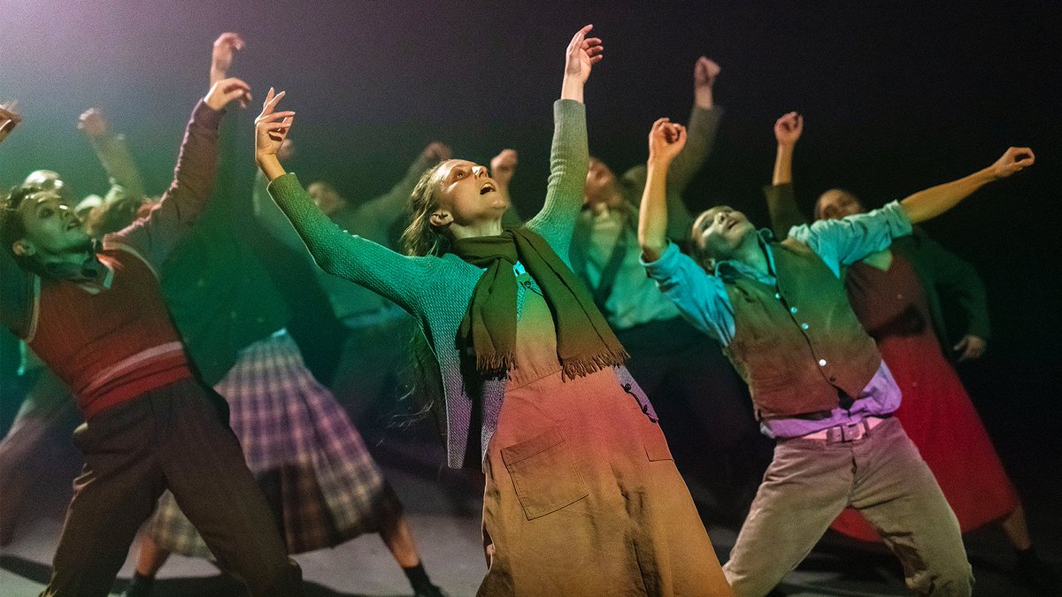 A group of people in knitwear and colourful clothing lean dramatically back with their hands in the air.