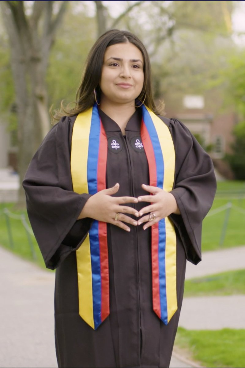 A student wears a graduation gown and a yellow, blue and red stole