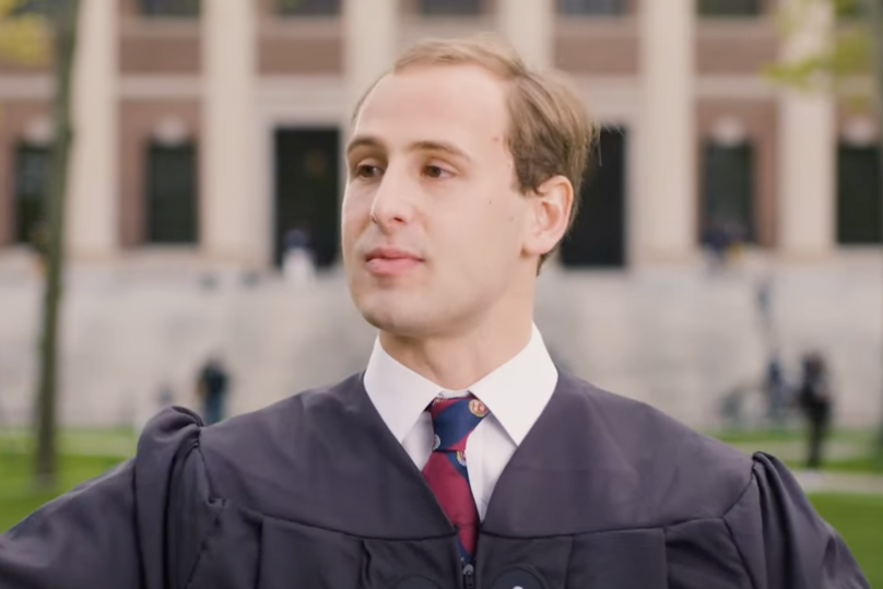 A graduate wearing a graduation gown holds his arms out wide 