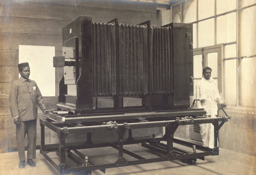 Two assistants standing beside a huge camera in the Photographic Department of the Survey of India.