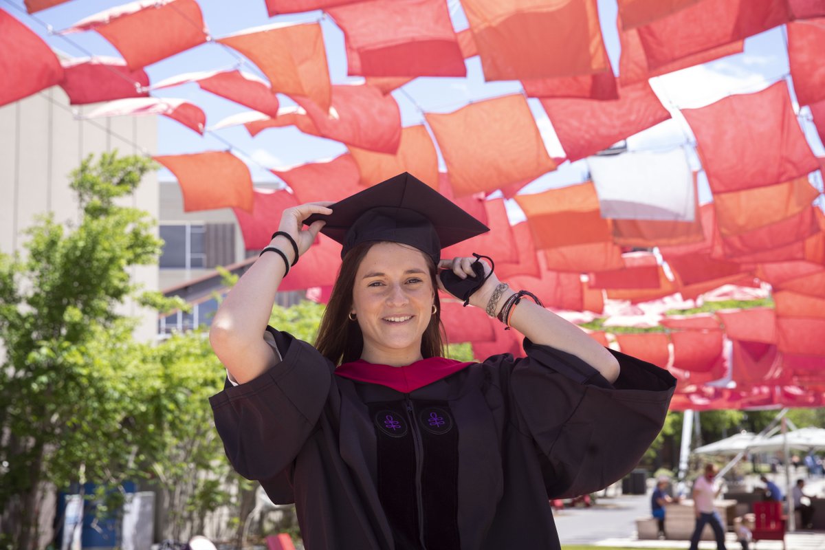 A graduate adjusts her cap while standing under red flags