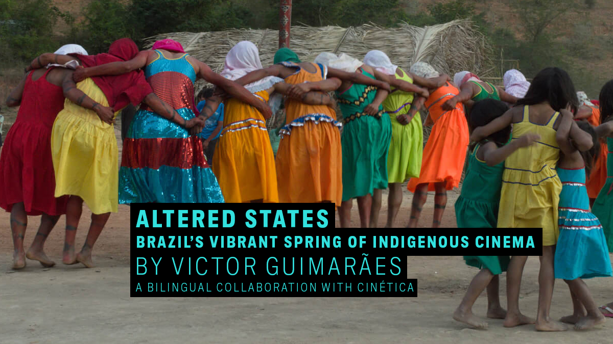A group of people clad in brightly colored dresses and skirts put their arms around each other while standing outside in a rural, hilly setting