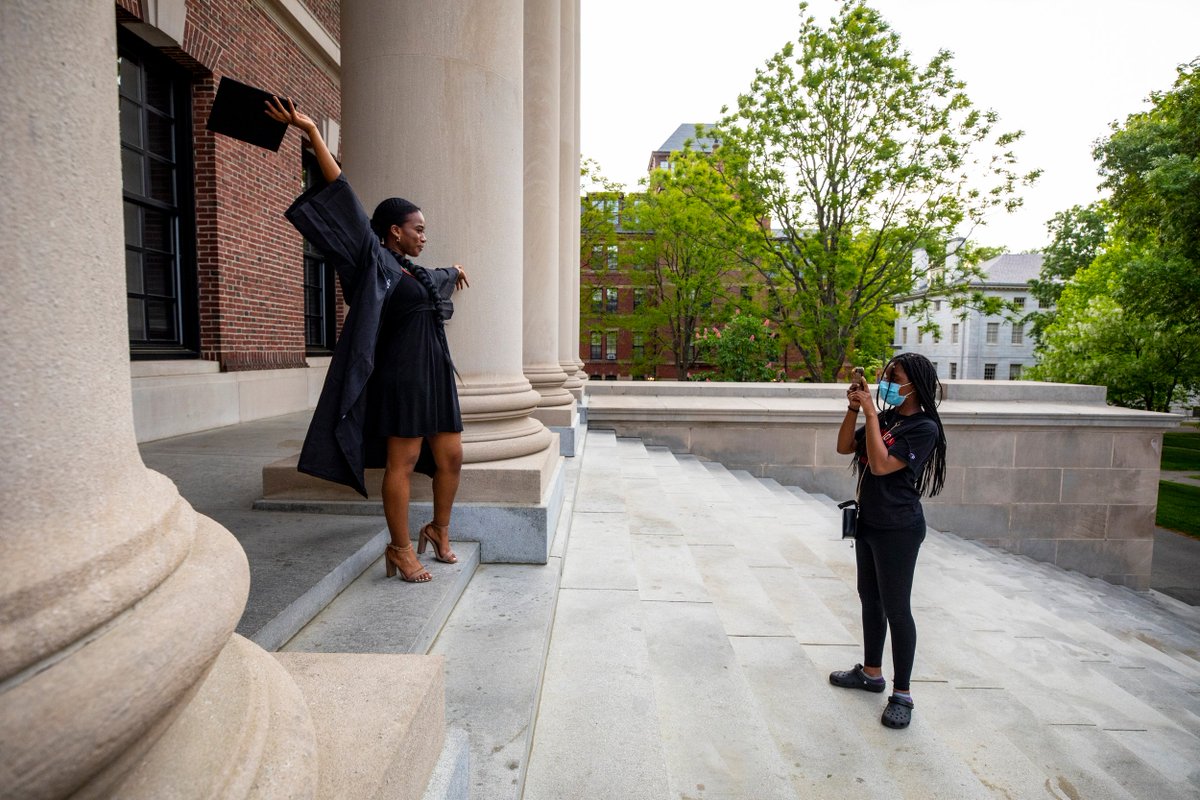 A woman takes a photo of a graduate on the steps of Widener Library