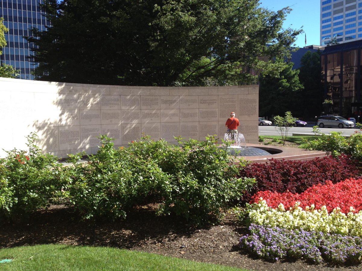 A man pauses at a large curved wall as he reads one of the many etched panels. Flower beds form the foreground.