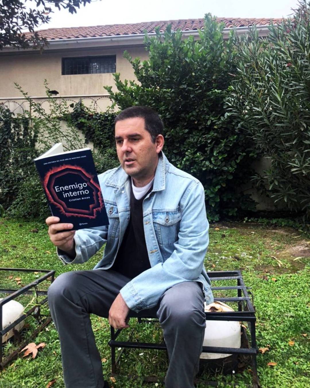 El periodista Cristian Arcos leyendo su nuevo libro "Enemigo interno" sentado en un patio.