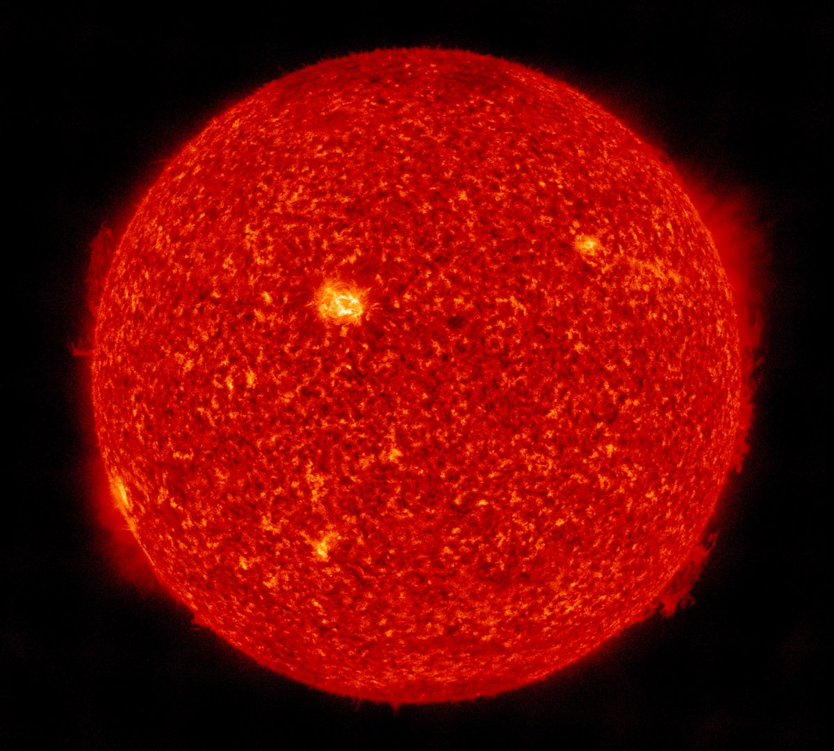Die erdzugewandte Seite der Sonne in warmer orangeroter Farbe. Am Rand einige kleinere Eruptionen - wie diffus ausgefranst wirkend. Die seit Tagen als hellerer Fleck erkennbare Aktive Region ist mitsamt der Rotation der Sonne etwas weiter nach rechts gewandert und jetzt nahezu mittig auf der Sonnenoberfläche. 