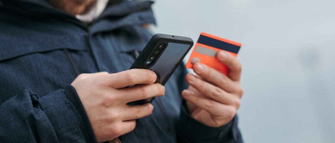 close-up photo of a man's hands holding a smartphone and credit card