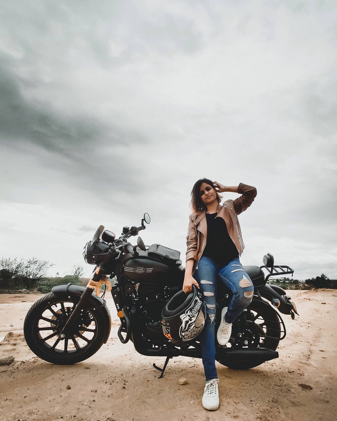 Photo of thoughtful Caucasian female likes riding motorbike, poses near her  fast bike, has leather jacket on shoulder, keeps hand on helmet, looks  aside with pensive expression, deep in thoughts Stock Photo |
