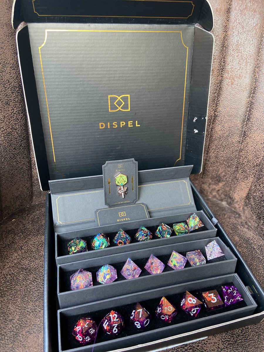 kellerator's tweet photo. THEY’RE HERE!!! Although the cat clearly didn’t get the “do not eat” memo and immediately went in for a chomp 😂. I guess I’m not the only dice goblin in this apartment!! (Don’t worry, no @dispeldice were harmed, only the poor box.) https://t.co/PuTh1QTHr7