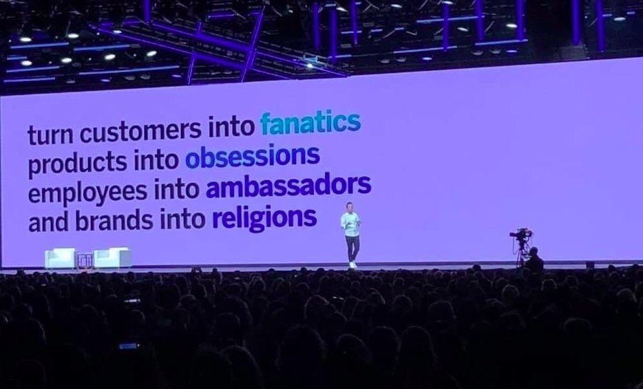 Guy on a stage at one of those big tech conference things.
Screen behind him says:
turn customers into fanatics 
products into obsessions
employees into ambassadors
and brands into religions 