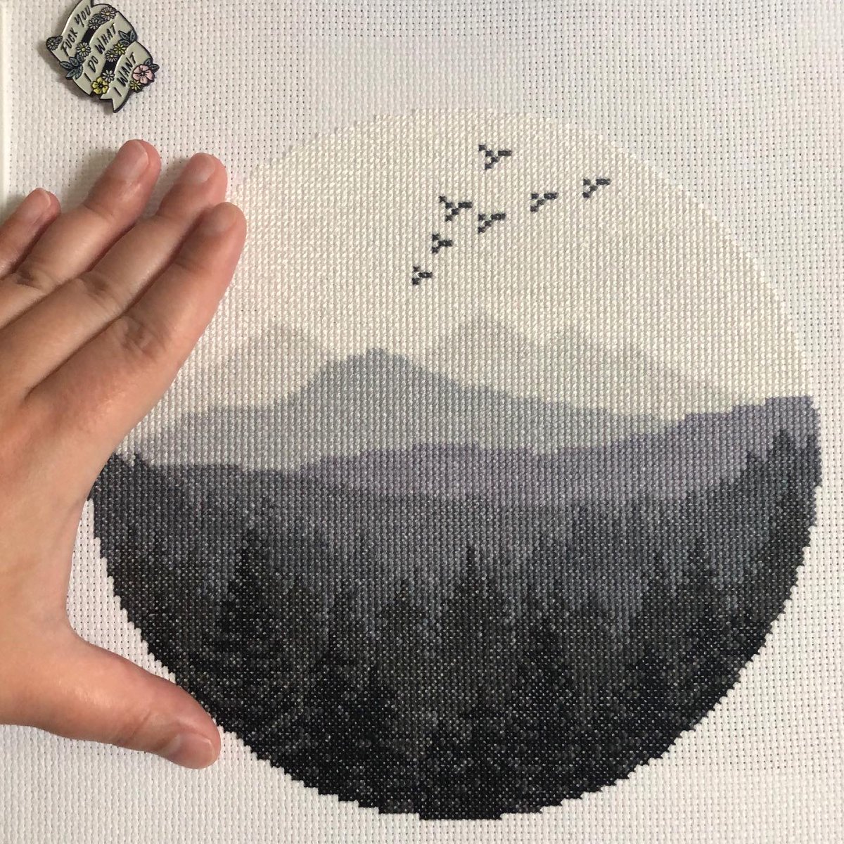 The same cross stitch with an open hand next to it for scale. The outstretched fingers reach only about two-thirds or three-quarters of the project’s total height. 