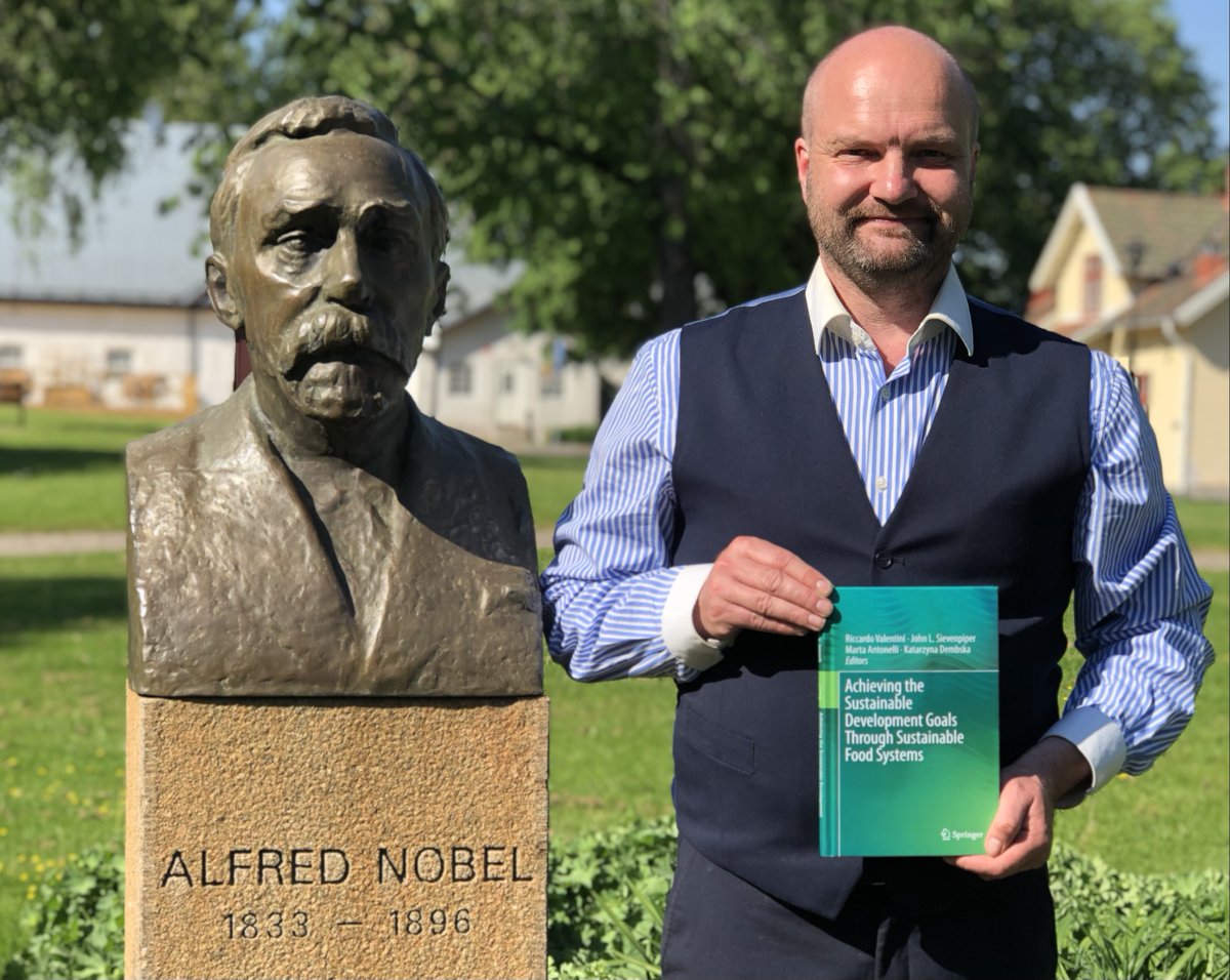 Man holding book next to bust of Alfred Nobel