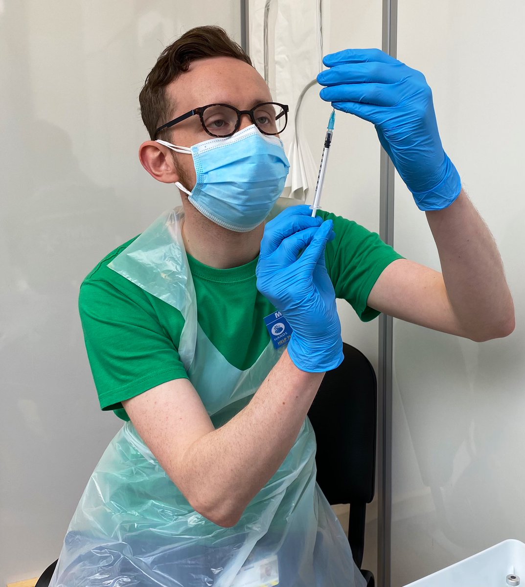 Matt being trained to draw up vaccine into a needle, wearing PPE.