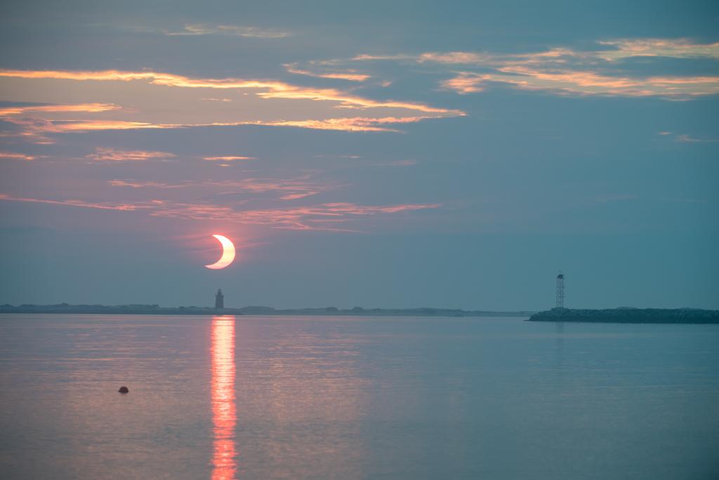 A partial solar eclipse is seen as the Sun rises behind the Delaware Breakwater Lighthouse