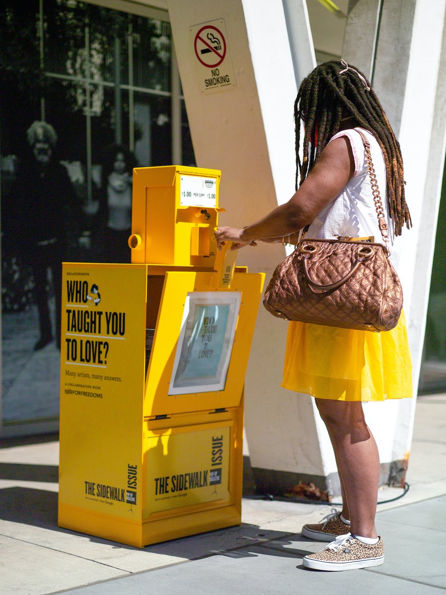 Person with long hair and yellow skirt opens a yellow newspaper box, to pick up a print edition of WHO TAUGHT YOU TO LOVE, a printed tabloid part of Pop-Up Magazine's Sidewalk Issue.