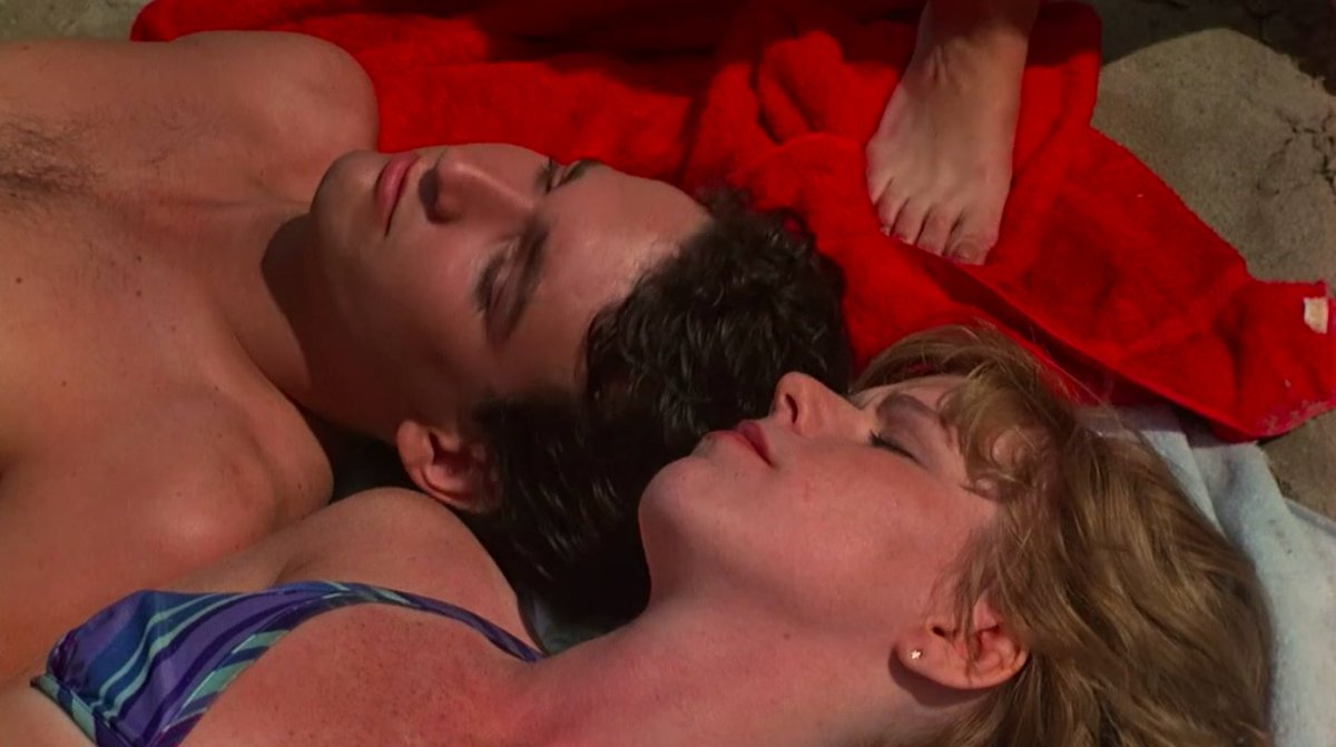 White teen boy and girl lying in the sun on towels. A person’s foot is in the background.