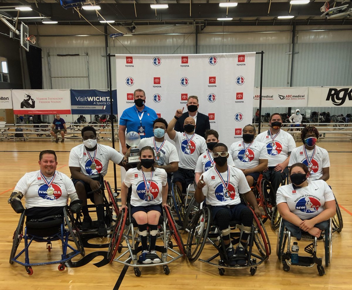 The Lakeshore Storm wheelchair basketball team wearing NWBA t-shirts and medals posing with the DIII championship trophy.