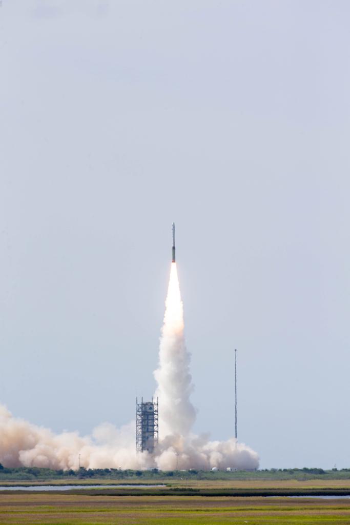 White and yellow rocket launching across a blue, cloudy sky.