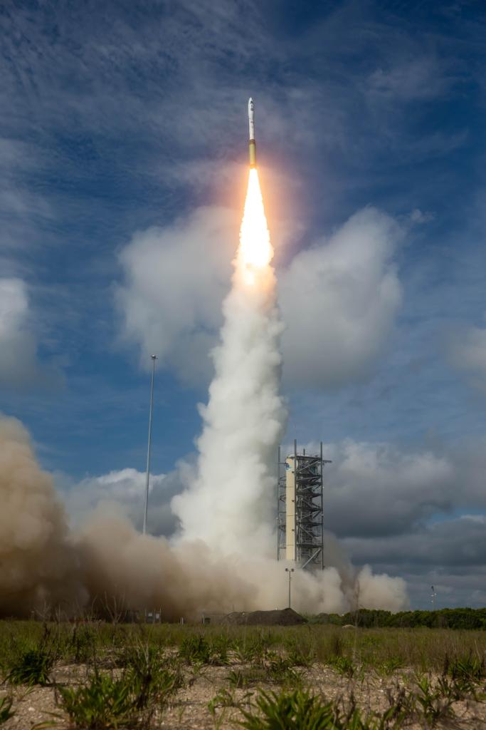 White and yellow rocket launching across a blue, cloudy sky.