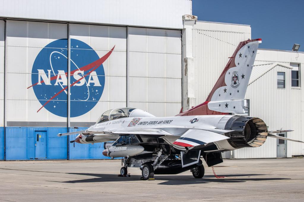 White, red and blue Thunderbird jet in front of hangar doors with NASA logo.