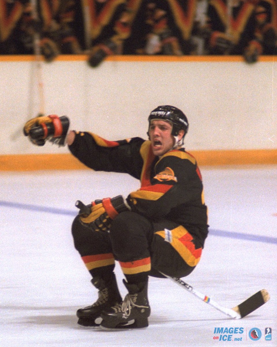 Tiger Williams of the Vancouver Canucks rides his stick as part of a goal celebration. He wears the classic black uniform with the yellow and orange V striping. 