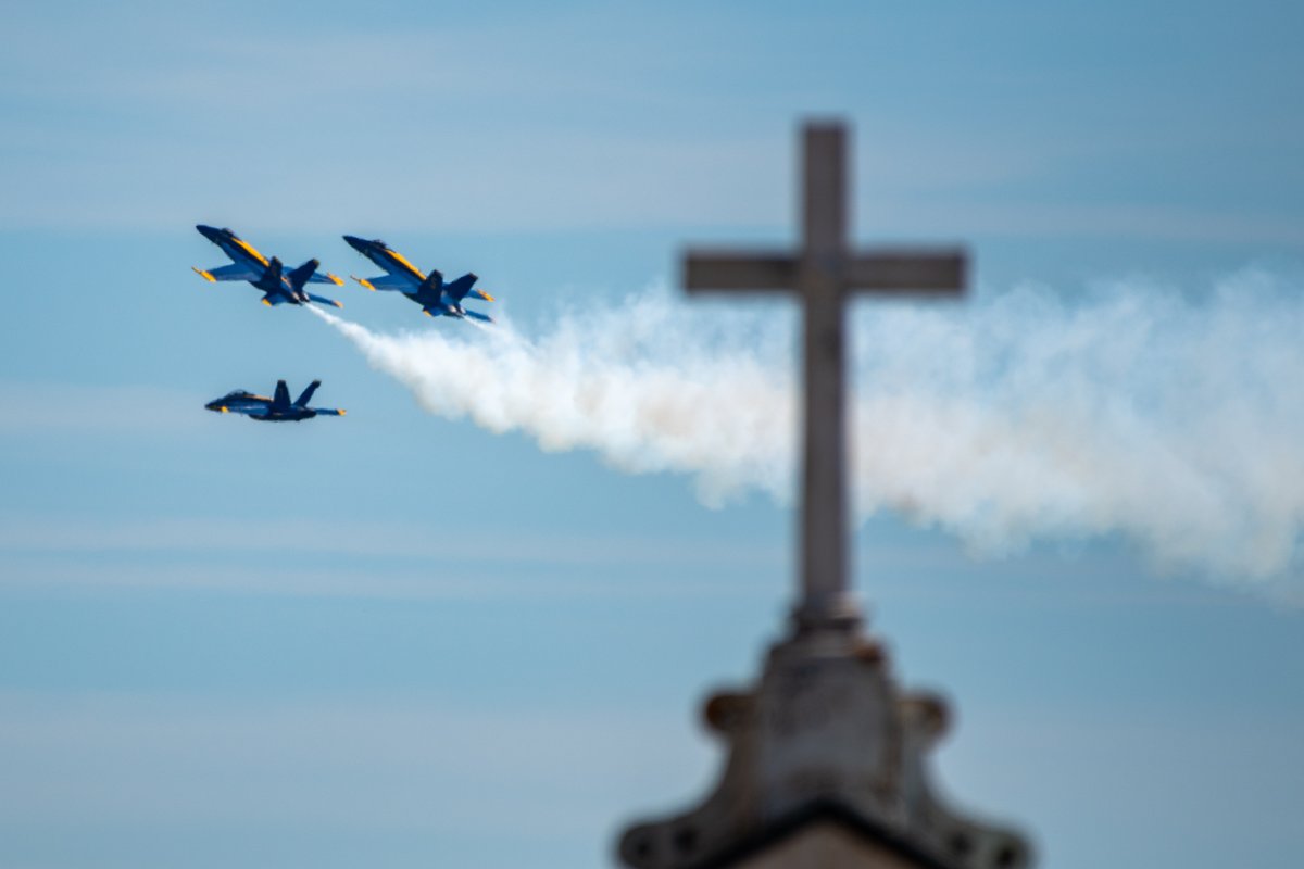 Three Blue Angels planes flying past a cross on top of a building.