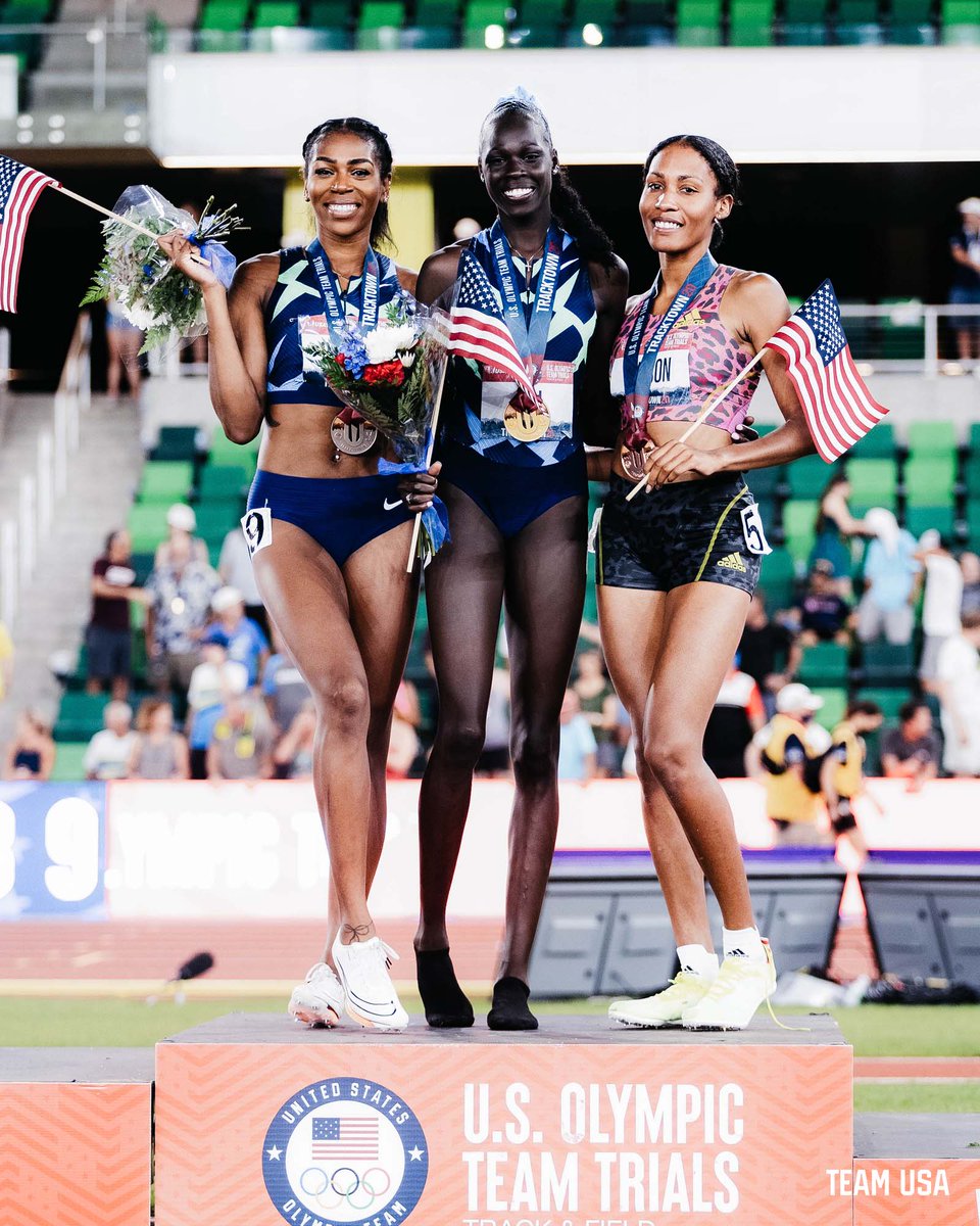 three athletes standing on a podium holding flags and bouquets and smiling