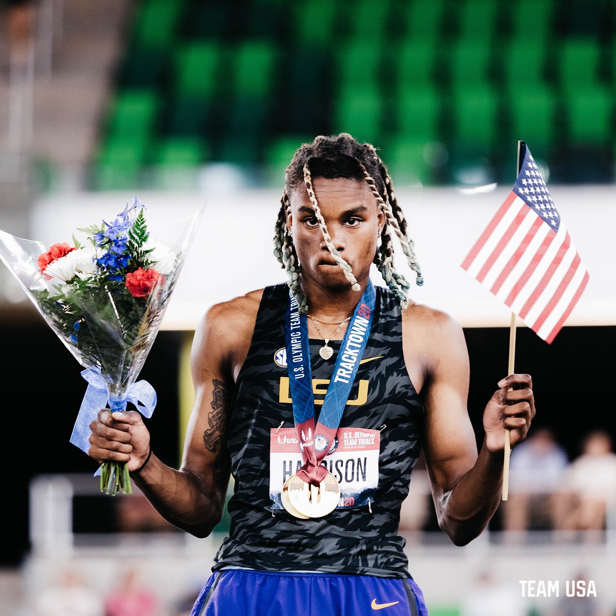 JuVaughn Harrison holding flowers and an American flag on the podium.