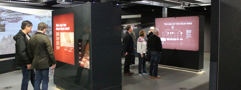 Visitors in the museum looking at displays, the house lights are up and make the room much lighter