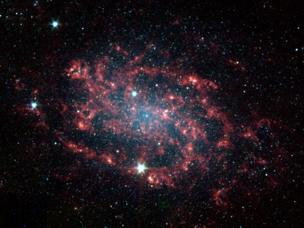Image of galaxy NGC 300, taken by the Spitzer Space Telescope. In the center there is a blue haze representing the greatest concentration of stars. Surrounding that are dusty spiral arms in red.