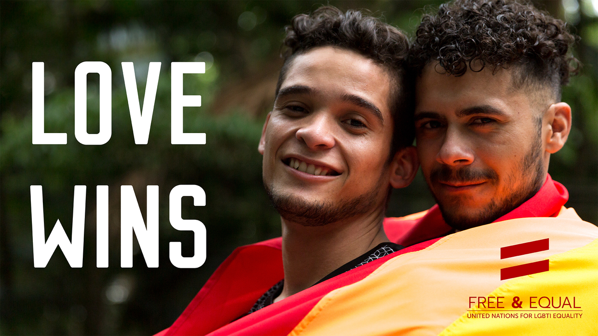 a couple of young people are standing close together wrapped in a rainbow flag; the tagline reads "love wins"