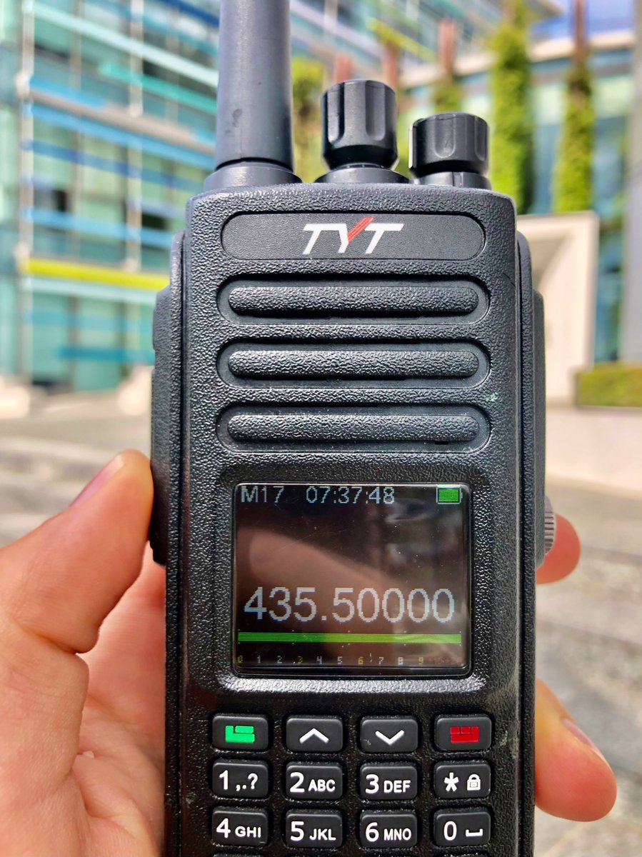 Picture of an MD-390 in IU2KIN’s hand, with OpenRTX M17 screen showing on the display. The radio is set on 435.500MHz, in the background there is a blurred commercial building.