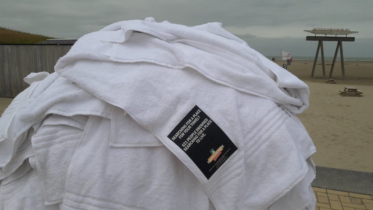 Bijzondere actie in #Zeebrugge-Bad, honderden figuren op het strand gemaakt, alsof ze zijn aangespoeld, witte badhanddoeken eroverheen gelegd met tekst Zoekt u een plek voor uw badhanddoek, 621 mensen verdronken op zoek naar een plek om te leven, #Vluchtelingenwerk #Vlaanderen.