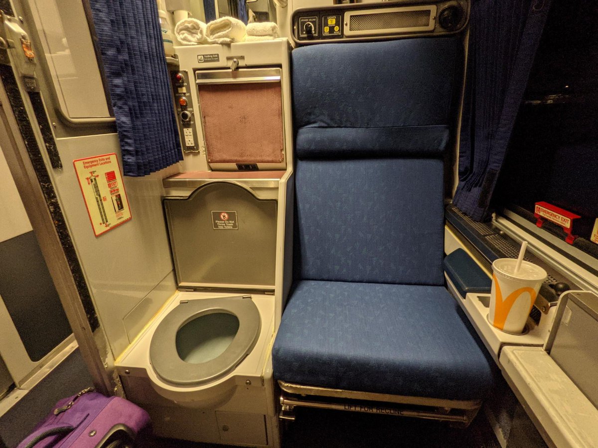 A toilet inside a train compartment, next to a regular seat.