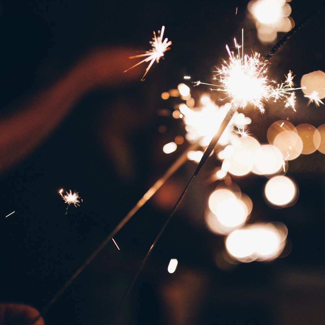 A hand-held lit sparkler with golden sparks lighting up the night sky