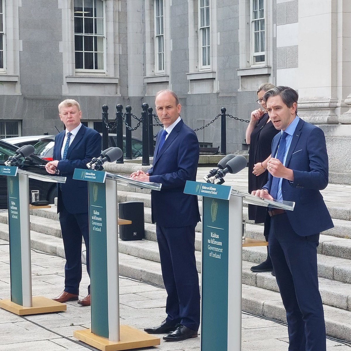 Photo shows Minister Harris speaking outside Government Buildings,  alongside the Taoiseach and Tim Conlon.