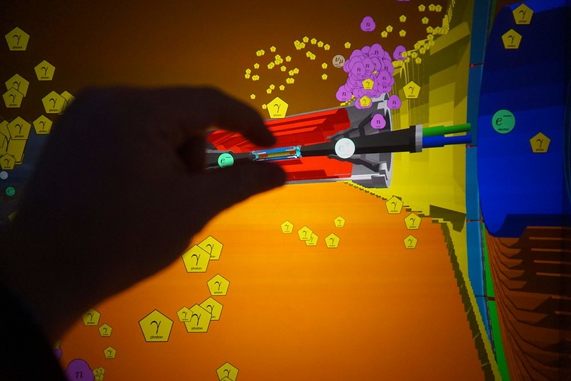 A hand trying to grasp an illustration of part of the Belle II accelerator.