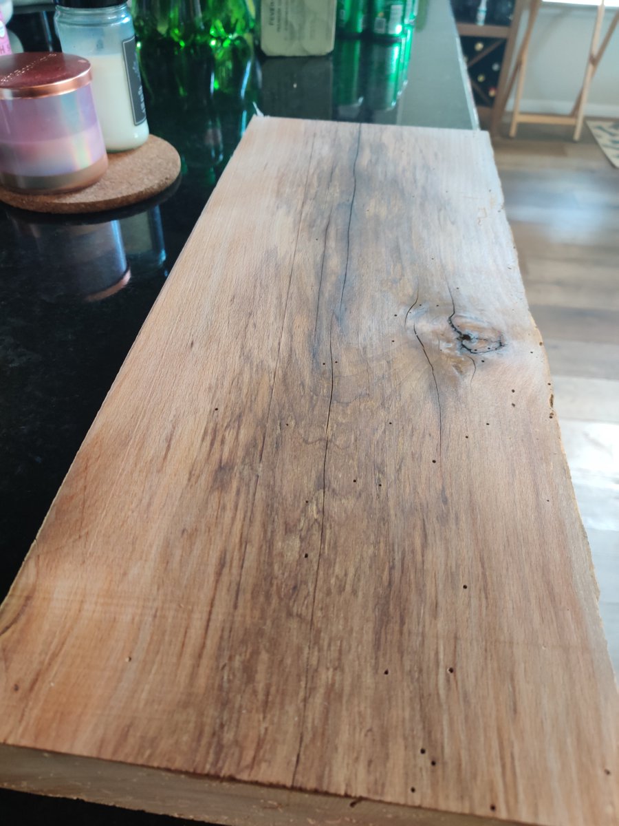 Thick piece of reclaimed wood sitting on a black countertop.  It is a buttery brown with streaking in the middle from age, and some small scattered bug holes