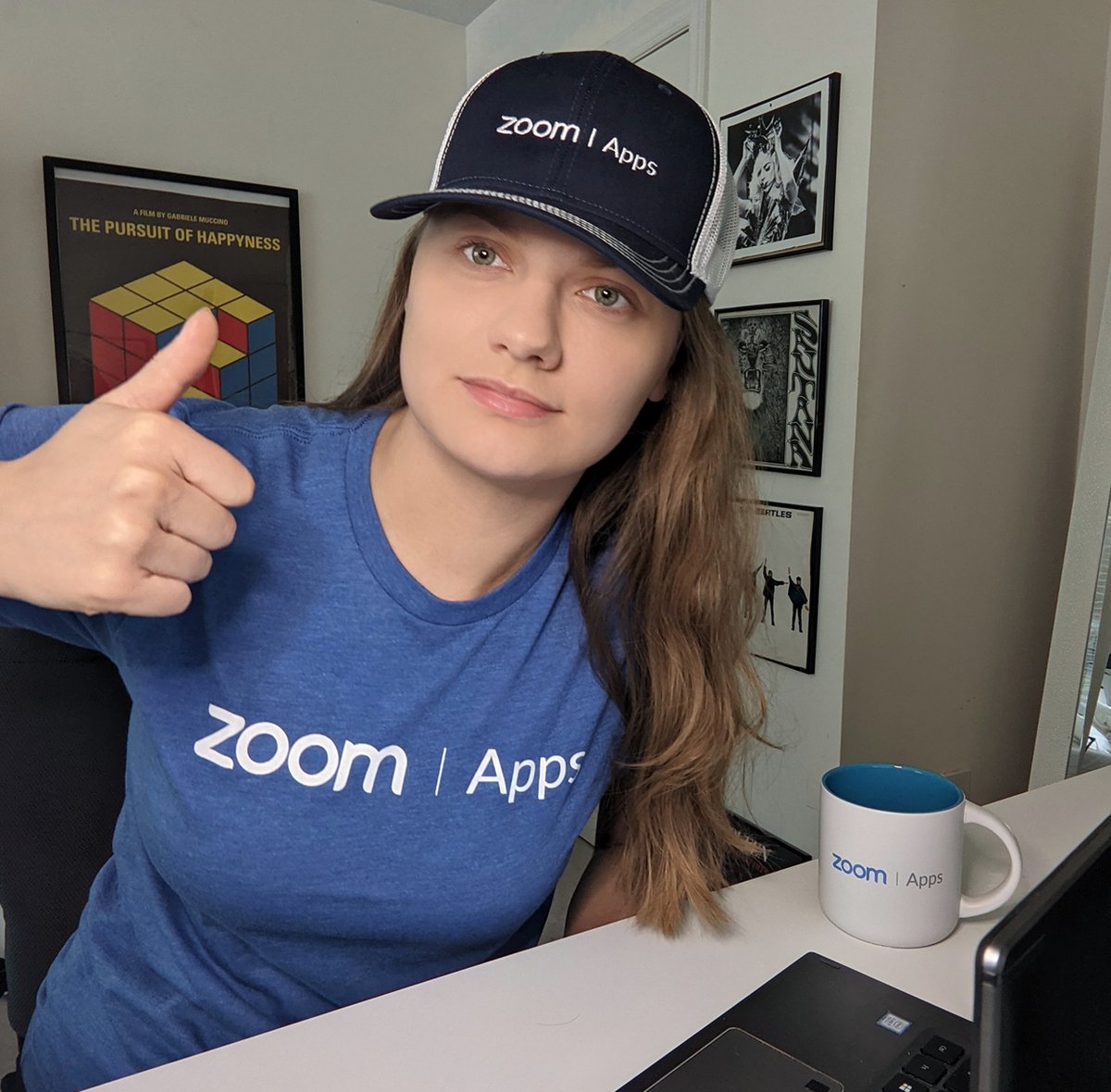 Photo of me wearing a Zoom Apps t-shirt, hat and mug, giving a thumbs up with my hand.