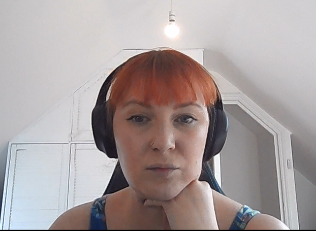 me, a ginger haired woman in her 30s looking at a webcam. behind her is some white built in cupboards and an open door