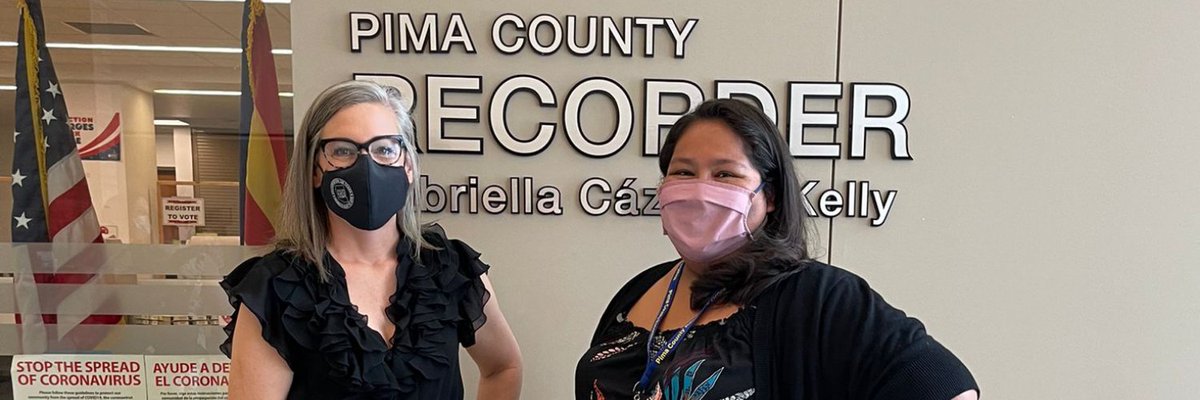 Image Description:  Picture of Arizona Secretary of State, Katie Hobbs and Pima County Recorder, Gabriella Cázares-Kelly standing in front of the Pima County Recorder’s office entrance, in the background is a wall sign that reads: “Pima County Recorder, Gabriella Cázares-Kelly” in shiny, metallic letters.