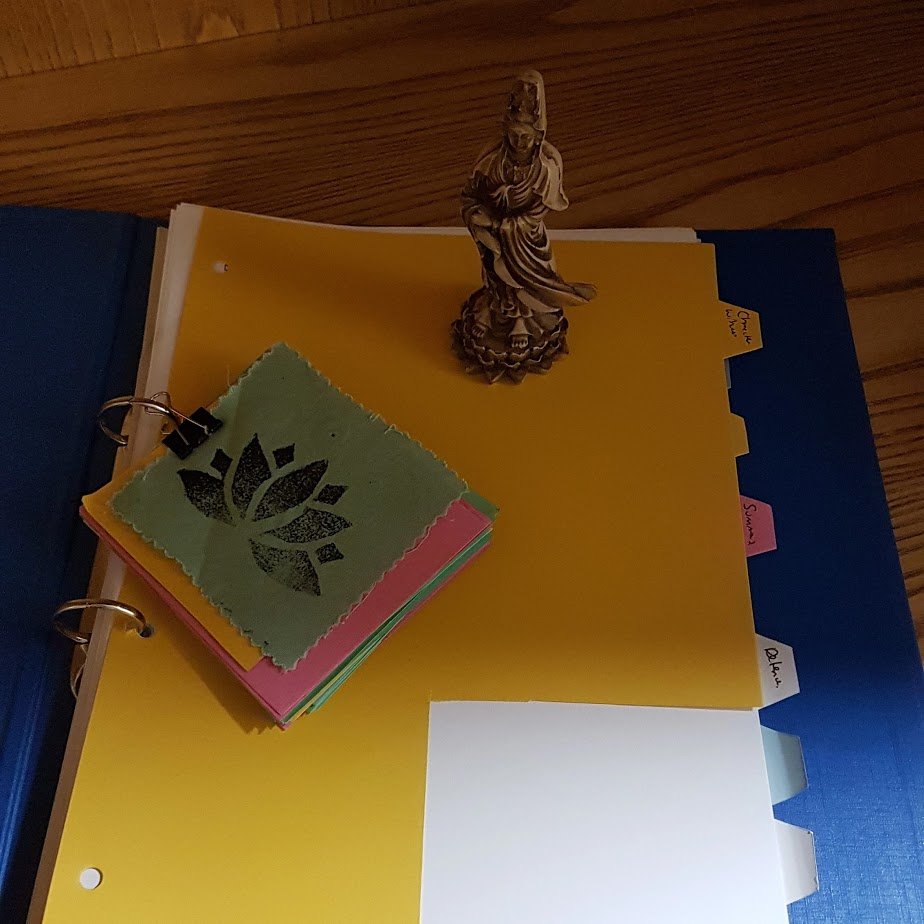 A folder with tabs on it.  There is a statue of Quan Yin on the folder and a number of coloured cue cards with a lotus patch all pinned together. 