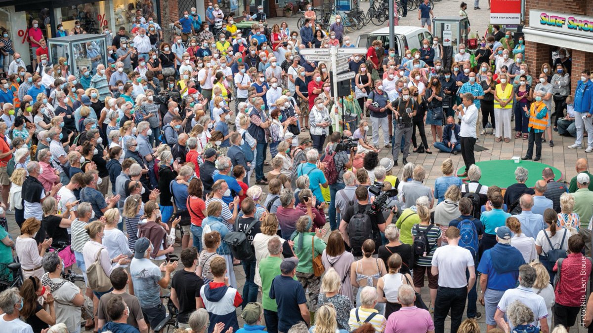 Robert Habeck ist auf einer grünen Bühne zu sehen. Um ihn herum stehen viele Menschen, die Masken tragen.