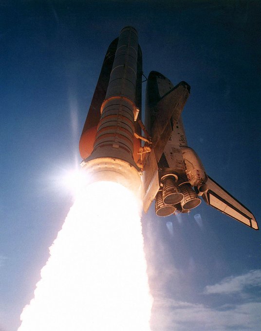 Photo of space shuttle launching from below, with column of fire coming out of the rockets