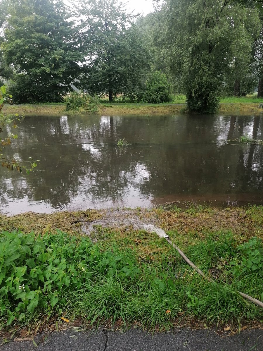 Die Niers, normalerweise ein kleiner Bach, führt starkes Hochwasser und ist kurz davor über die Ufer zu treten. Ein Feuerwehrschlauch pumpt Wasser von einem Grundstück in den Fluss