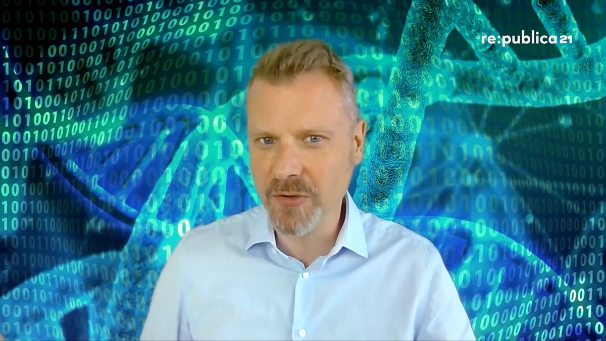 Screenshot aus der rp21-Session von Christian Stöcker „KI und Biotech: Hier kommt die nächste Beschleunigung“: Christian Stöcker vor einer bildschirmfüllenden Grafik auf der Nullen und Einsen und ein DNS-Strang in blau-grünen Farbtönen abgebildet sind.