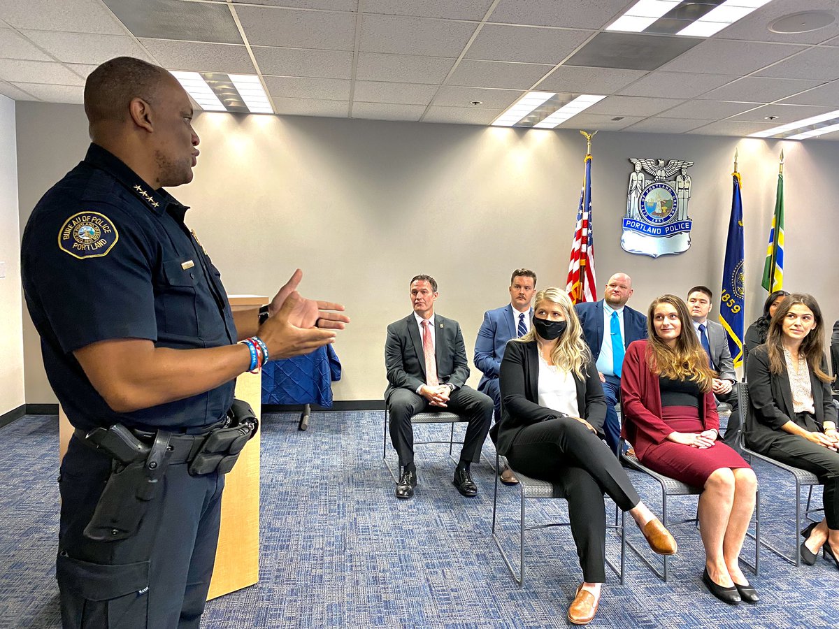Chief Lovell, standing, addresses newly hired officers seated at the front of the room.