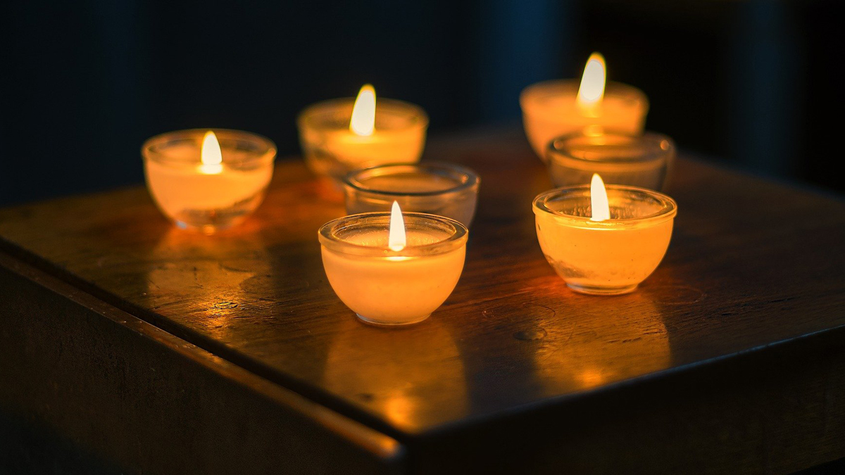 Auf dem Bild sind im Dunkeln leuchtende Kerzen zu sehen, die auf einem Tisch stehen.