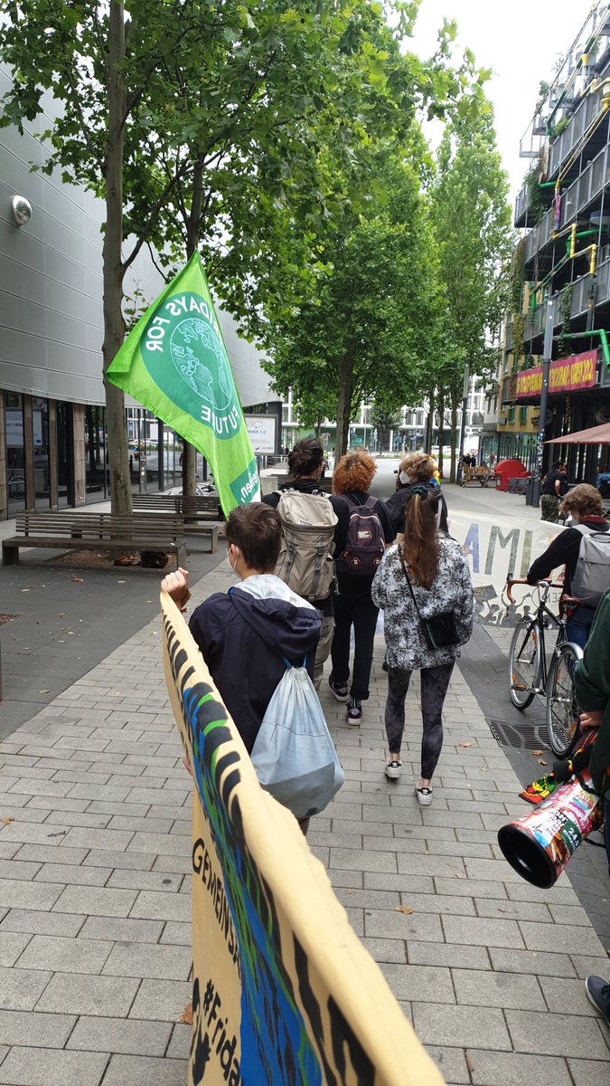 Eine Laufdemonstration in einer Fußgängerzone in Essen, zu sehen aus der Demo heraus. Gut zu sehen ist eine Fridays-for-Future-Fahne unter grünen Baumkronen.